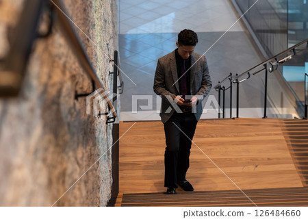 Walking down office staircase, businessman checking smartphone in modern setting 126484660