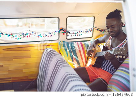 Man playing guitar inside colorful van, enjoying music and relaxing on road trip, copy space 126484668
