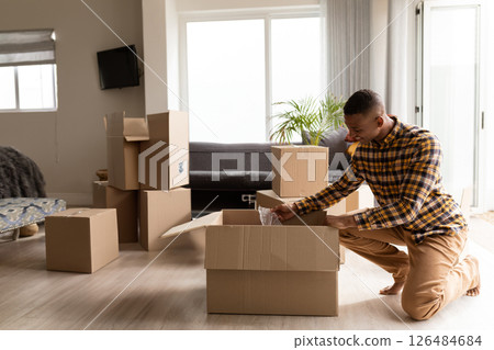Man unpacking boxes in living room, organizing new home with care, copy space Man unpacking boxes in living room, organizing new home with care, copy space 126484684