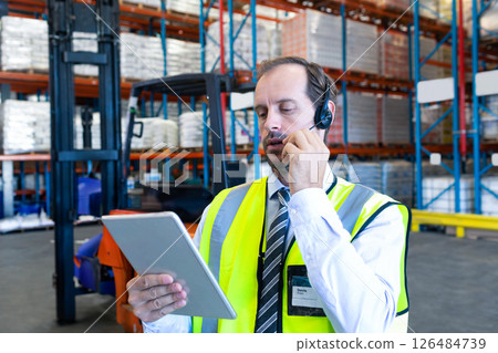 Using tablet and headset, warehouse manager managing inventory and communicating Using tablet and headset, warehouse manager managing inventory and communicating 126484739