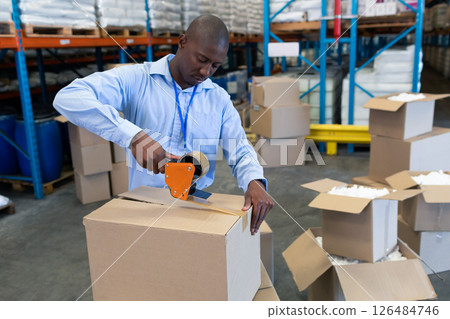 Warehouse worker sealing cardboard box with tape dispenser, focusing on task, copy space 126484746