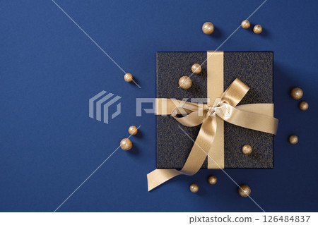 Dark blue gift box with gold ribbon and decorations on a blue background. Space for your text. 126484837