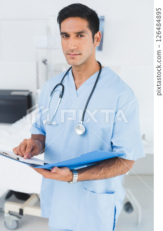 In hospital, medical professional in scrubs reviewing patient chart with stethoscope 126484895