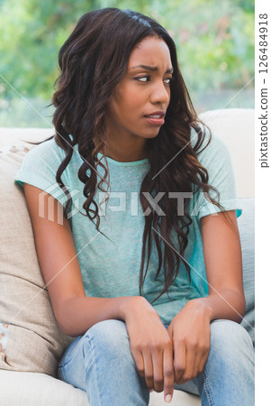 Thoughtful woman sitting on sofa at home, looking away in contemplation 126484918