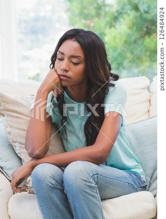 Thoughtful woman sitting on couch at home, looking pensive and relaxed 126484924