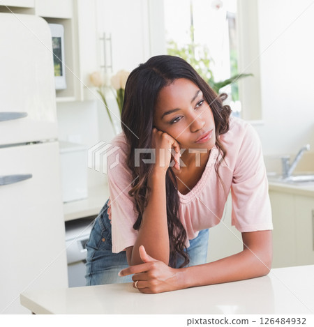 Woman leaning on kitchen counter, daydreaming in bright, modern kitchen 126484932