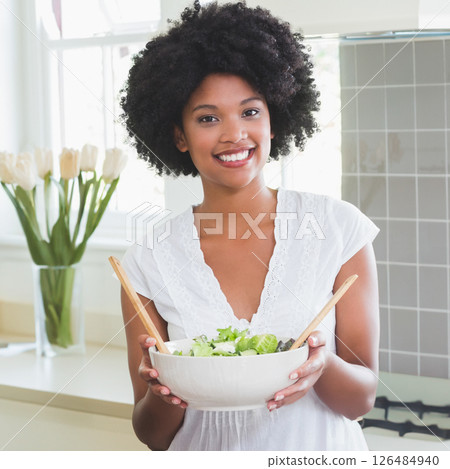Smiling woman holding fresh salad in kitchen, enjoying healthy lifestyle Smiling woman holding fresh salad in kitchen, enjoying healthy lifestyle 126484940