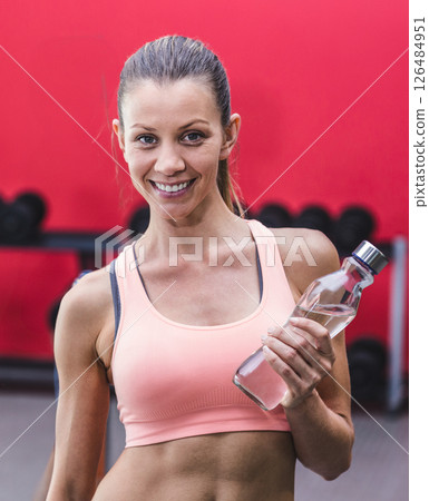 Smiling woman holding water bottle in gym, ready for workout session Smiling woman holding water bottle in gym, ready for workout session 126484951