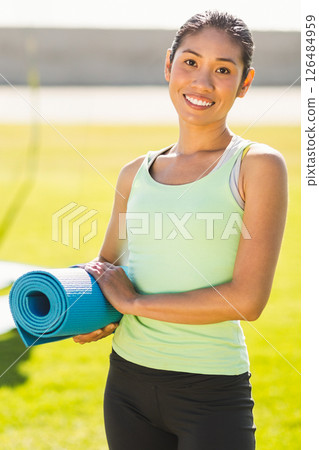 Smiling woman holding yoga mat outdoors, ready for morning exercise routine 126484959