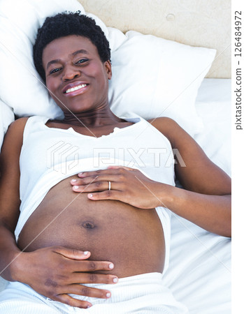 Pregnant woman relaxing on bed, smiling and embracing her belly with joy Pregnant woman relaxing on bed, smiling and embracing her belly with joy 126484972