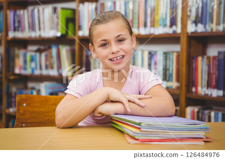 Smiling girl sitting in school library with colorful books on table 126484976
