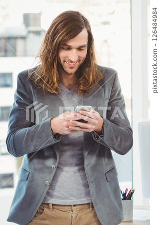 Casual hipster smiling while texting on smartphone in modern office 126484984