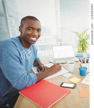 Smiling man working at desk with laptop, coffee, and colorful stationery 126484987