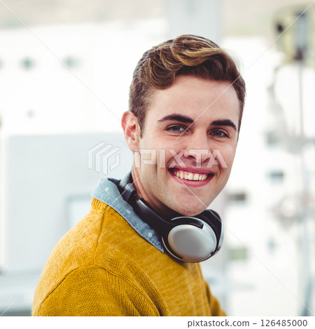 Smiling young man with headphones working in modern office environment 126485000