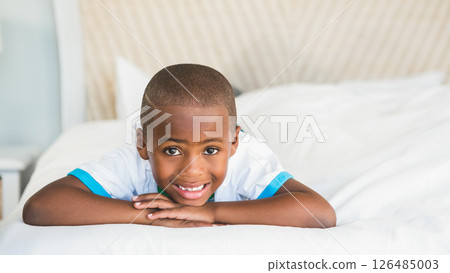 Smiling African American boy relaxing on bed at home, feeling happy and content 126485003