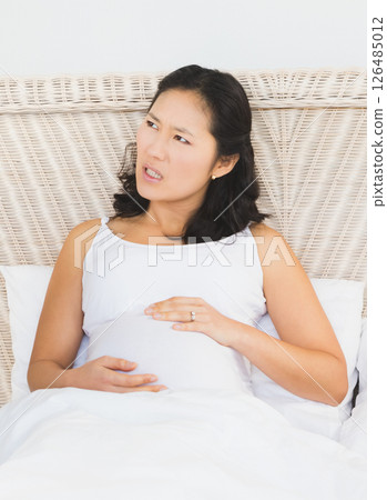 Pregnant Asian woman resting in bed, looking thoughtful and relaxed at home 126485012
