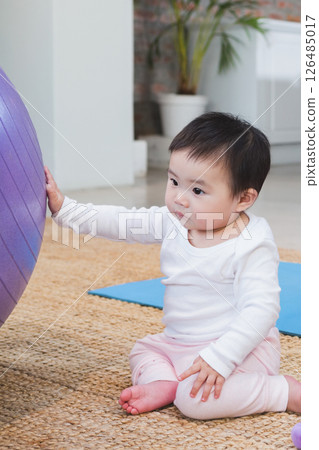 Asian baby playing with exercise ball on floor at home, looking curious 126485017