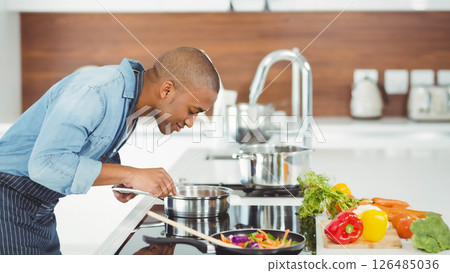 Man cooking in modern kitchen, checking pot with fresh vegetables nearby Man cooking in modern kitchen, checking pot with fresh vegetables nearby 126485036