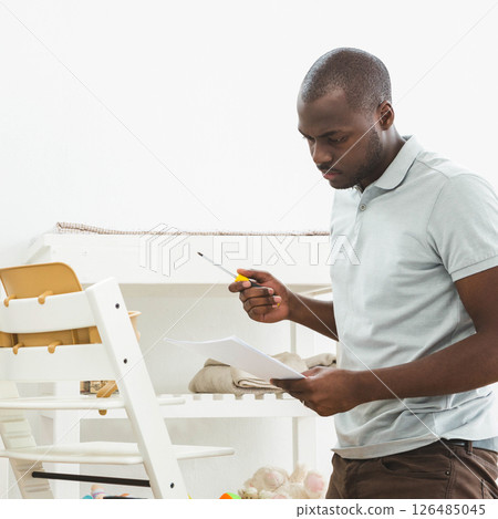 Father assembling baby furniture at home, focused on instructions and tools, copy space 126485045