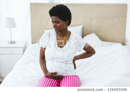 Pregnant woman sitting on bed, holding back, feeling discomfort at home 126485046