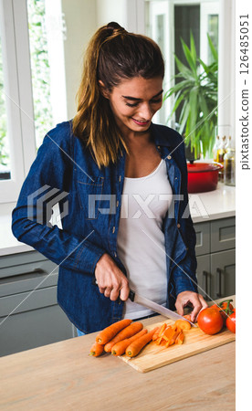 Smiling woman chopping carrots in kitchen, preparing fresh ingredients for cooking 126485051