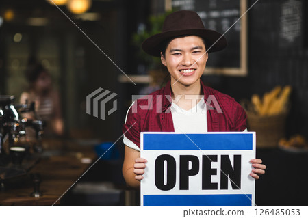 Smiling Asian man holding Open sign in cozy coffee shop Smiling Asian man holding Open sign in cozy coffee shop 126485053