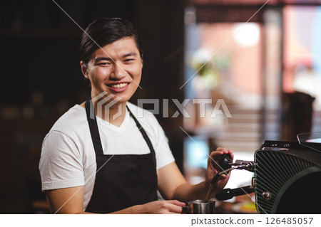 Barista in coffee shop smiling while preparing espresso with machine 126485057