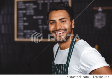 Smiling barista in apron welcoming customers at cozy coffee shop counter Smiling barista in apron welcoming customers at cozy coffee shop counter 126485063