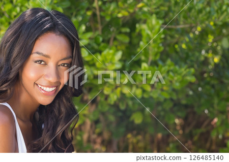 Smiling woman enjoying sunny day outdoors with lush green background, copy space 126485140