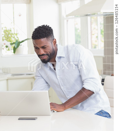 African American man using laptop in kitchen, smiling and working from home African American man using laptop in kitchen, smiling and working from home 126485154