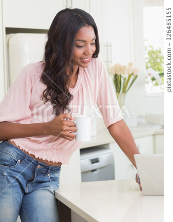 African American woman enjoying coffee while using laptop in bright kitchen 126485155