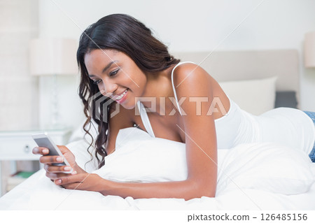 African American woman smiling while using smartphone in cozy bedroom 126485156