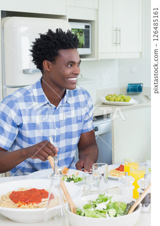 Smiling man enjoying pasta meal in bright kitchen, feeling happy and relaxed 126485161