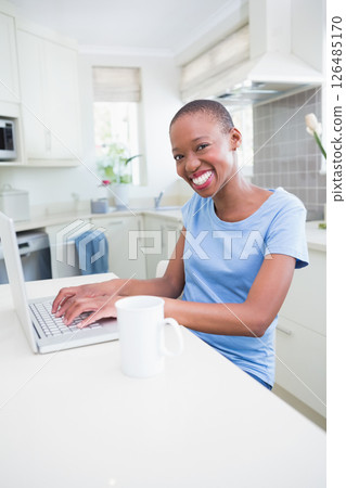 African American woman smiling while using laptop in bright kitchen 126485170