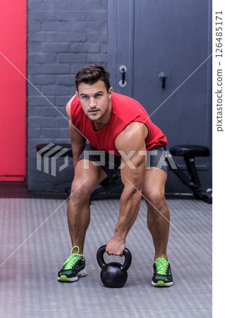 Man lifting kettlebell in gym, focused on strength training exercise 126485171