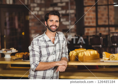 Smiling man in plaid shirt standing at bakery counter with pastries 126485184