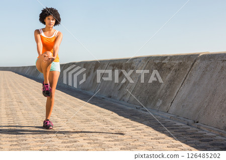 Woman stretching leg on sunny promenade, preparing for morning exercise outdoors, copy space Woman stretching leg on sunny promenade, preparing for morning exercise outdoors, copy space 126485202
