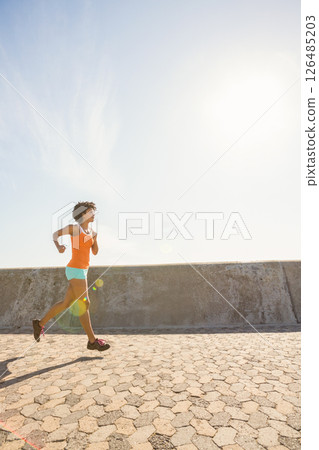 Woman jogging on sunny promenade, embracing morning fitness and vitality, copy space 126485203