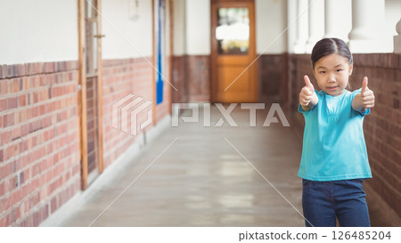 School hallway, young girl giving thumbs up, feeling confident and happy, copy space 126485204