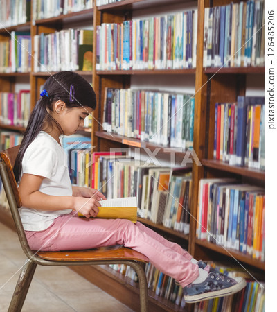 Young girl reading book in school library, sitting and concentrating on pages Young girl reading book in school library, sitting and concentrating on pages 126485206