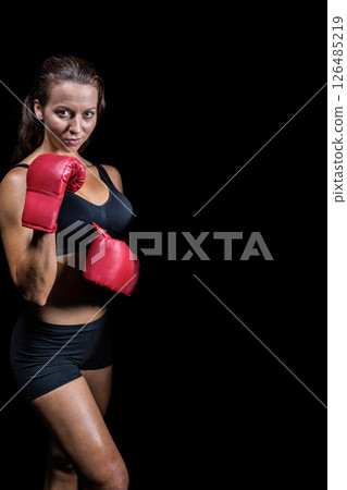 Confident woman in red boxing gloves posing against black background, copy space Confident woman in red boxing gloves posing against black background, copy space 126485219