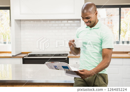 In kitchen, man reading newspaper while drinking coffee and smiling, copy space In kitchen, man reading newspaper while drinking coffee and smiling, copy space 126485224