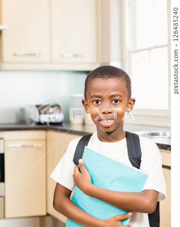Smiling boy with backpack holding book in kitchen, ready for school, copy space Smiling boy with backpack holding book in kitchen, ready for school, copy space 126485240