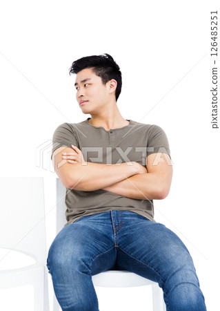 Asian man sitting on chair with arms crossed, looking to side 126485251