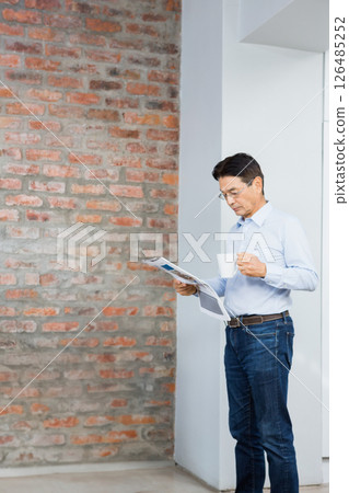 Asian man reading newspaper and drinking coffee at home, enjoying morning routine, copy space Asian man reading newspaper and drinking coffee at home, enjoying morning routine, copy space 126485252
