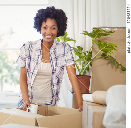 African American woman unpacking boxes at home, smiling and holding coffee cup African American woman unpacking boxes at home, smiling and holding coffee cup 126485254