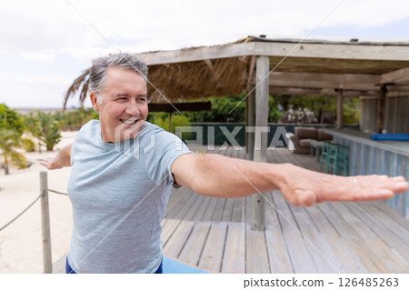 Smiling man practicing yoga on wooden deck at beachside retreat, copy space Smiling man practicing yoga on wooden deck at beachside retreat, copy space 126485263