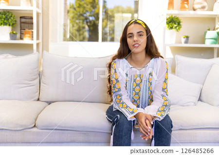 Woman sitting on couch at home, wearing colorful blouse, looking relaxed, copy space Woman sitting on couch at home, wearing colorful blouse, looking relaxed, copy space 126485266