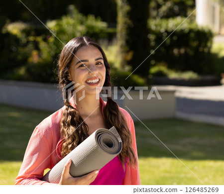 Smiling woman holding yoga mat outdoors, ready for exercise in garden, copy space Smiling woman holding yoga mat outdoors, ready for exercise in garden, copy space 126485269
