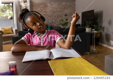 Young girl wearing headphones studying at home, engaging with her homework, copy space Young girl wearing headphones studying at home, engaging with her homework, copy space 126485283